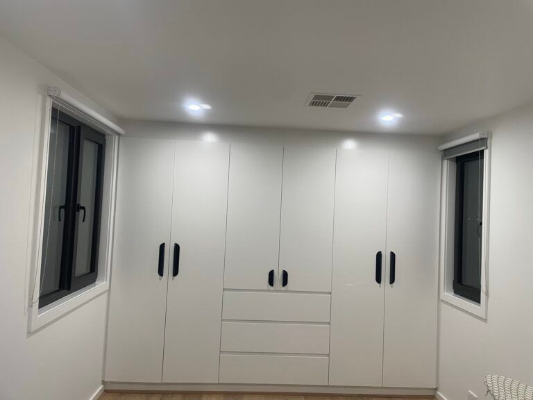 Built-in white wardrobe cabinetry with drawers beside two windows