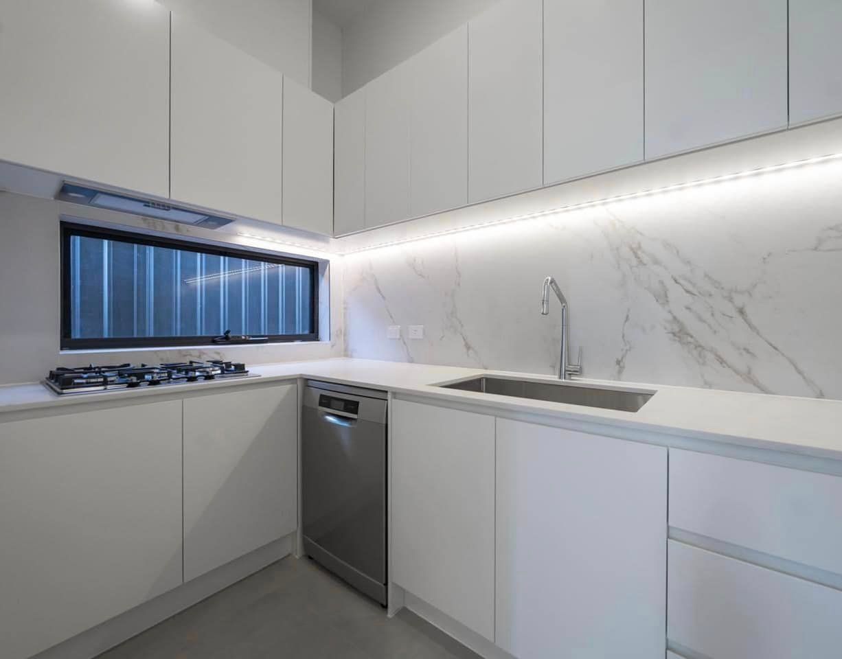 White kitchen cabinetry arranged around a sink, cooktop and window