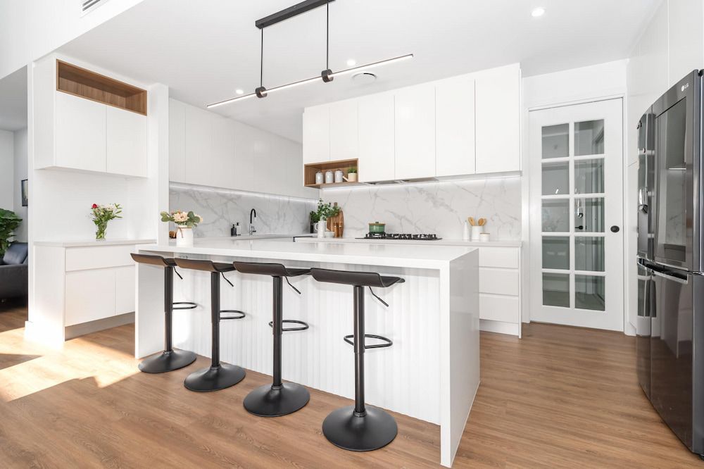 White kitchen cabinetry with black stools at the island